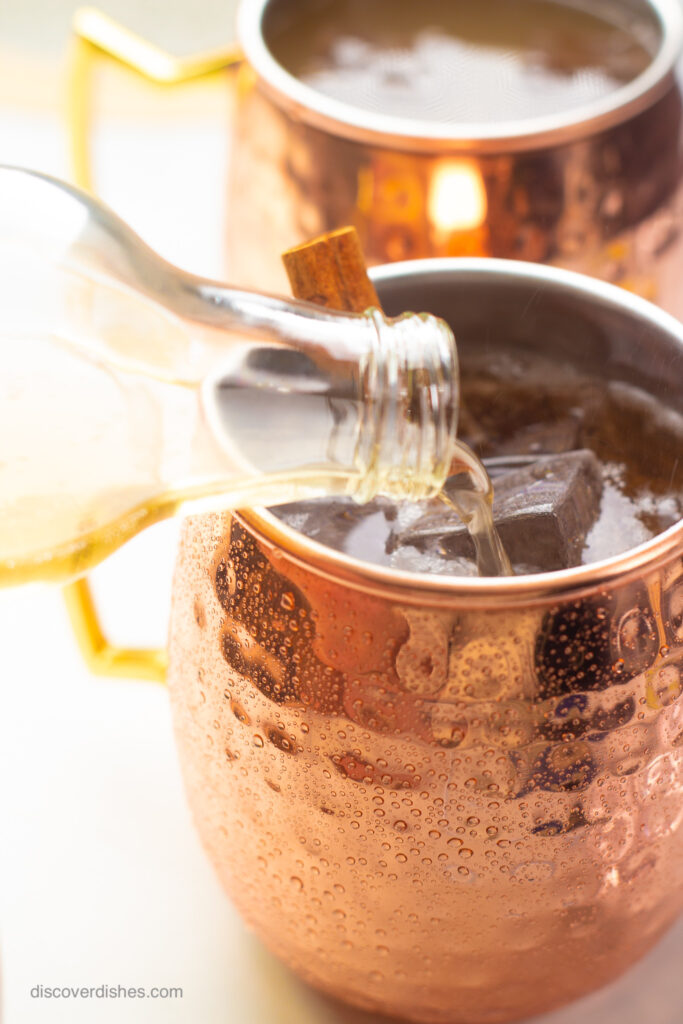 A bottle of ginger beer being poured into a copper mug.