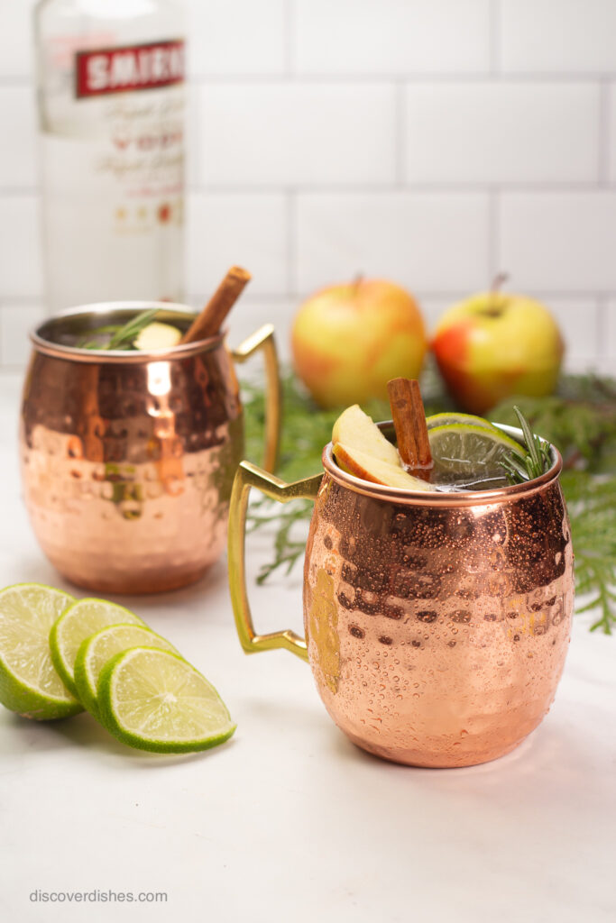 Two copper mugs filled with moscow mules and garnished with cinnamon sticks.