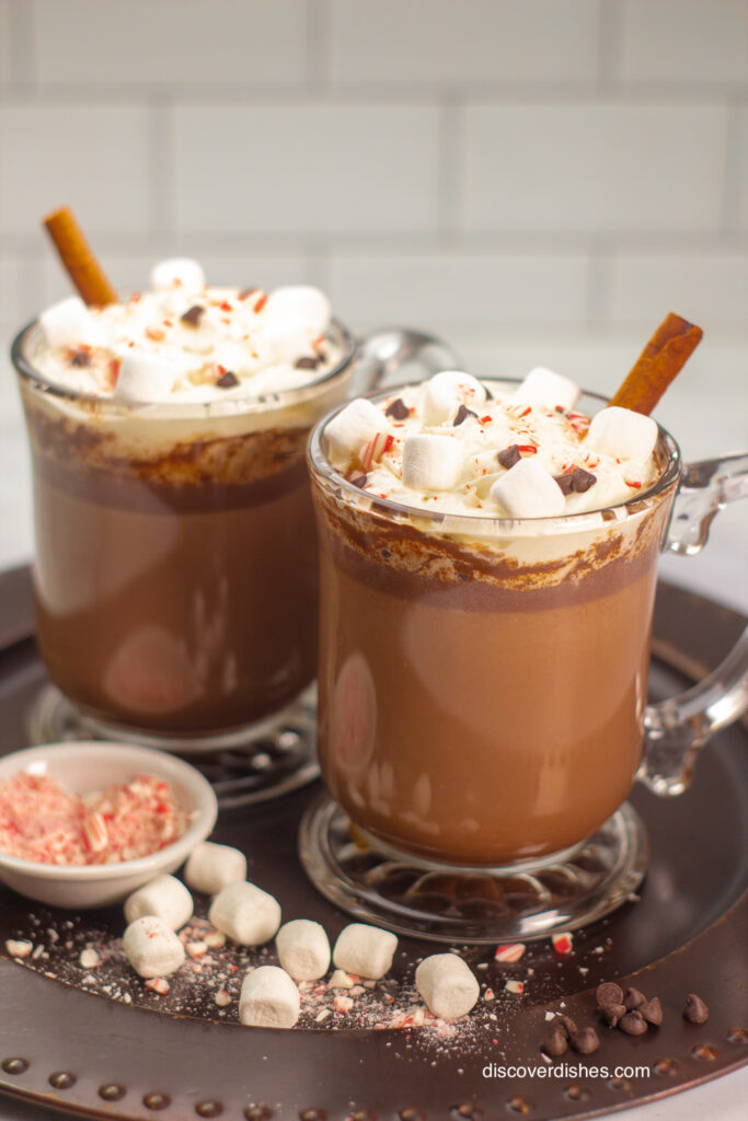 Two cups of mexican hot chocolate with garnishes on a platter.