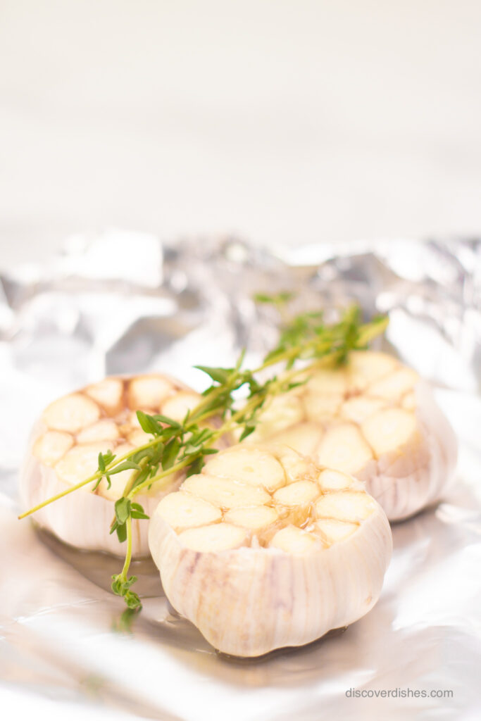 Garlic heads topped with time in aluminum foil.