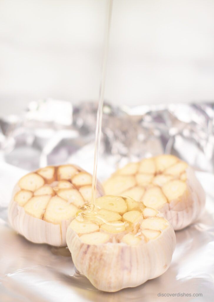 Olive oil being drizzled on heads of garlic.